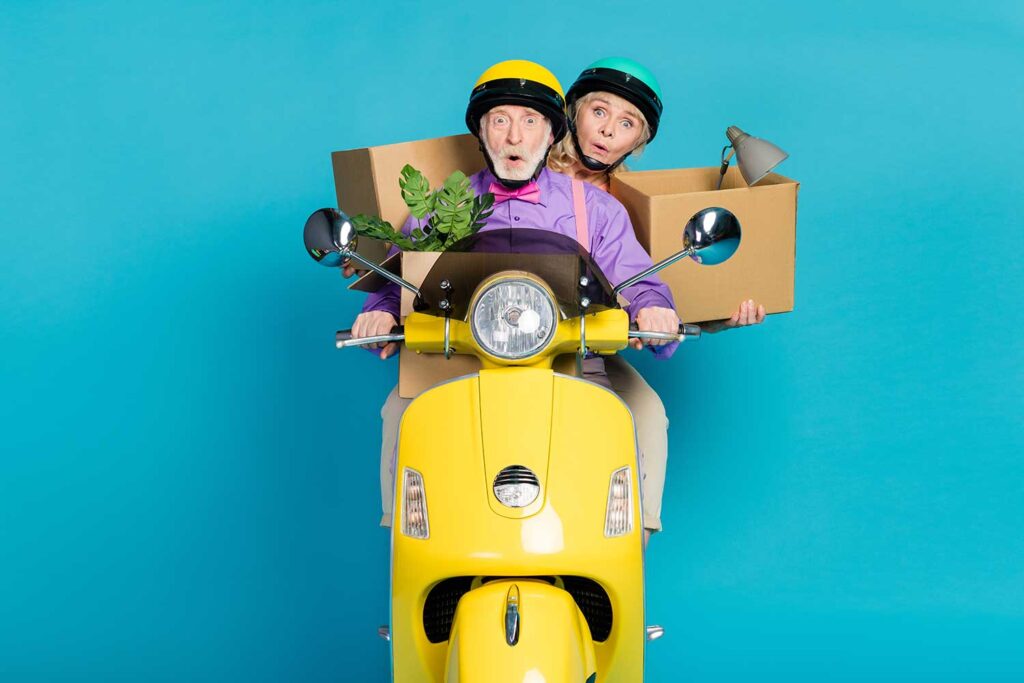 portrait humoristique d'un couple de seniors transportant des cartons de déménagement sur un scooter